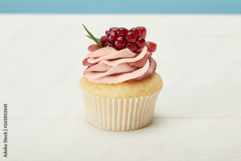 tasty cupcake with garnet and cream on white surface isolated on blue tasty cupcake with garnet and cream on white surface isolated on blue