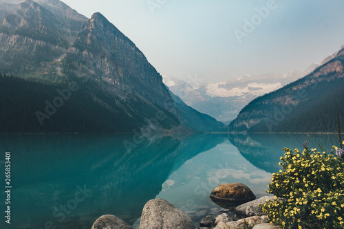 ein türkisfarbener See im Nebel mit gelben Blumen im Vordergrund  photo