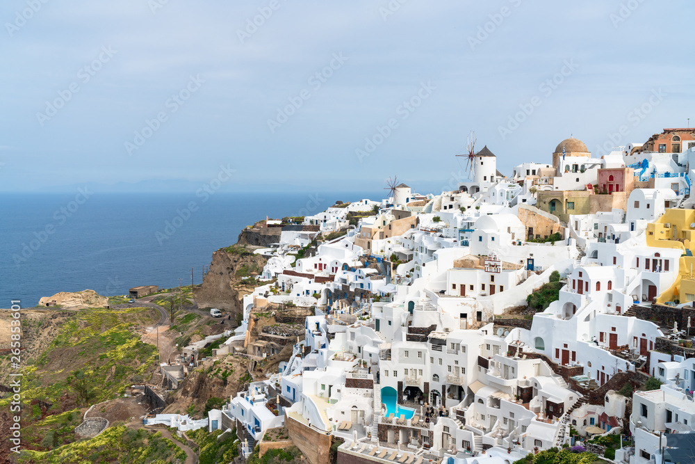 View of Oia, a coastal town on Greek island Santorini. The town has whitewashed houses carved into the rugged clifftops, and overlooks a vast caldera filled with water.