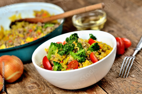 Bowl with tuna risotto with vegetables, tomatoes, broccoli and parsley, onions and oil in the background