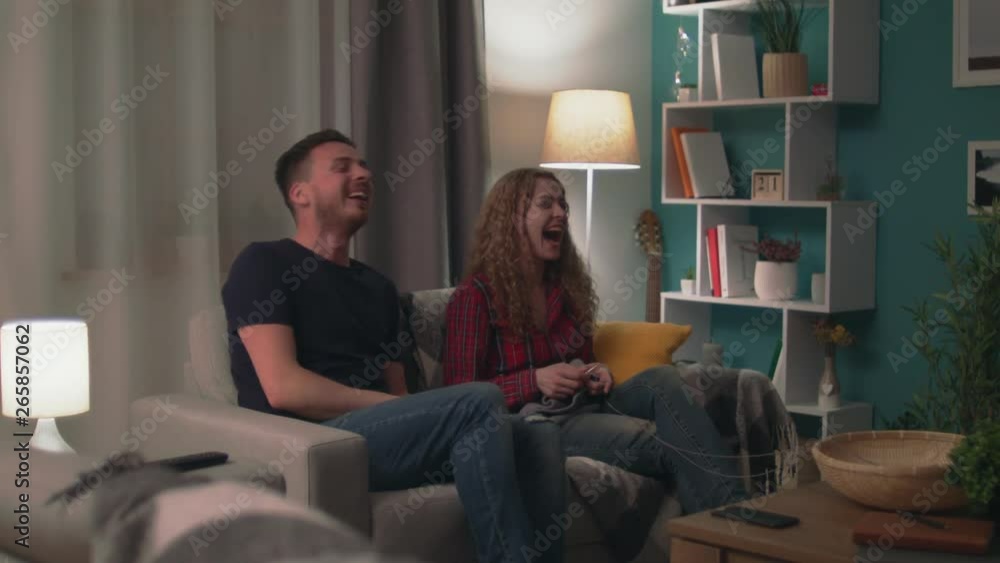 Panning of young happy couple sitting on sofa have fun chatting and laughing Panning of young happy couple sitting on sofa have fun chatting and laughing