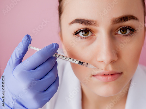 Doctor in gloves giving woman botox injections in lips, on pink background