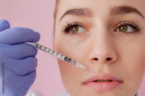 Doctor in gloves giving woman botox injections in lips  on pink background