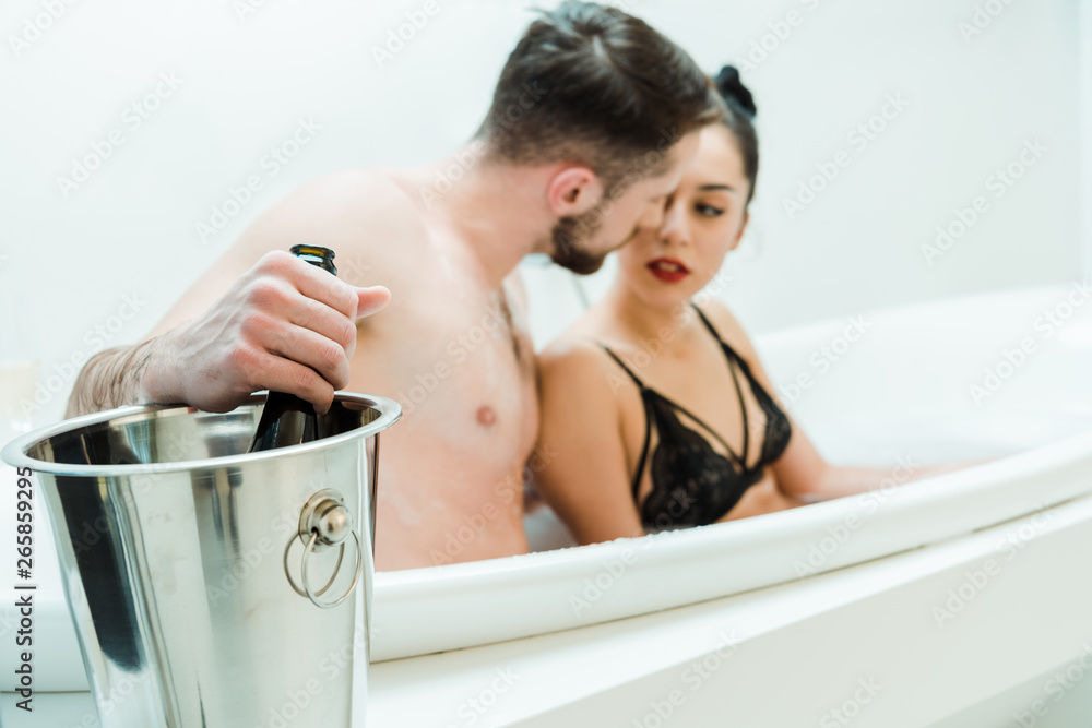 Obraz premium selective focus of man holding bottle of champagne near woman in bathtub