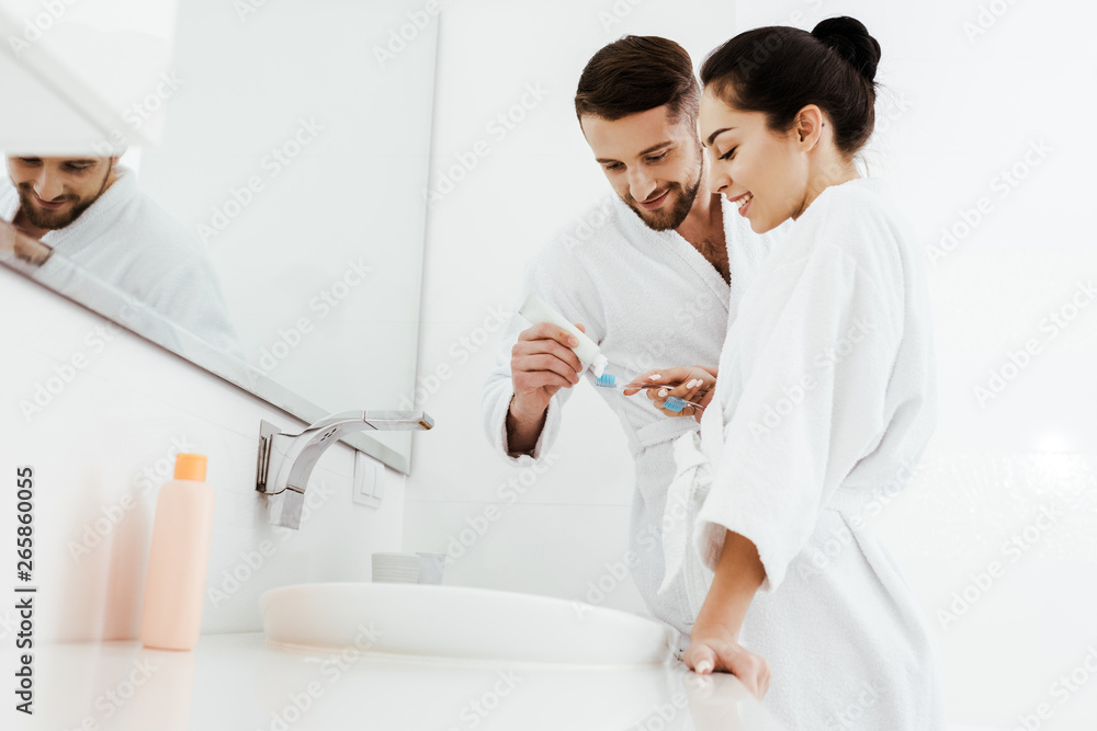 low angle view of cheerful woman looking at man holding toothbrush and toothpaste low angle view of cheerful woman looking at man holding toothbrush and toothpaste
