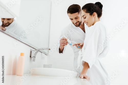 low angle view of cheerful woman looking at man holding toothbrush and toothpaste