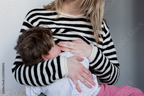 Young mother breastfeeding toddler boy in striped sweater