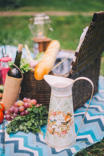 Close-up picnic in nature. Jug and food - greens, tomatoes, grapes, wine, baguette on the background of a picnic basket and a blue plaid