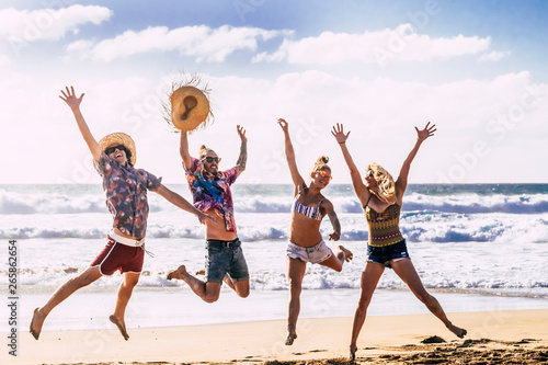 Summer holiday vacation travel concept with young group of people friends jumping for happiness and joy at the beach with blue sea and sky in background enjoying nature and outdoor free 