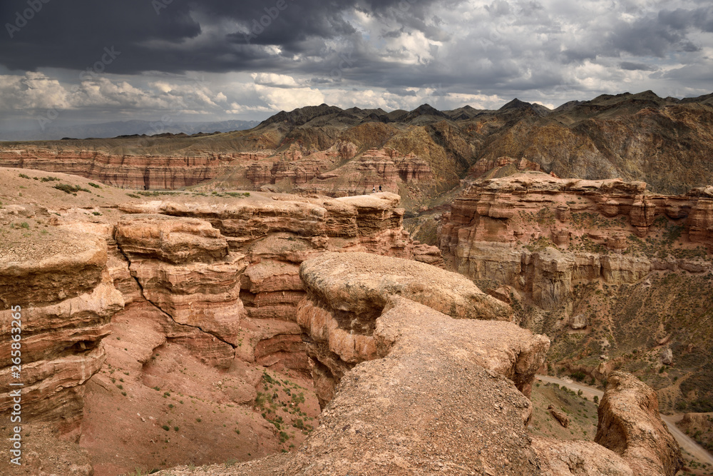 Tourists on cliff top at Charyn Canyon Park with clouds and Tien Shen mountains Kazakhstan