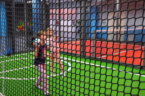 Blurred children are playing behind the net at indoor playground in activity park.