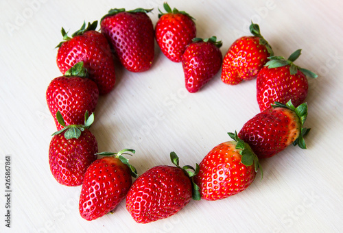 Fresh strawberries on the white wooden background, copy space. Strawberries heart. Sweet, juicy, ripe strawberries. Harvest of organic red strawberries. Delicious and healthy food. Vitamin-rich food. 