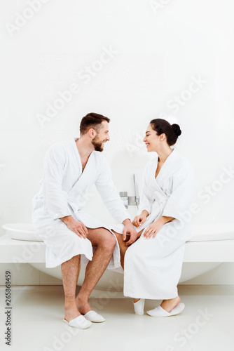 happy bearded man sitting and looking at attractive woman in bathrobe