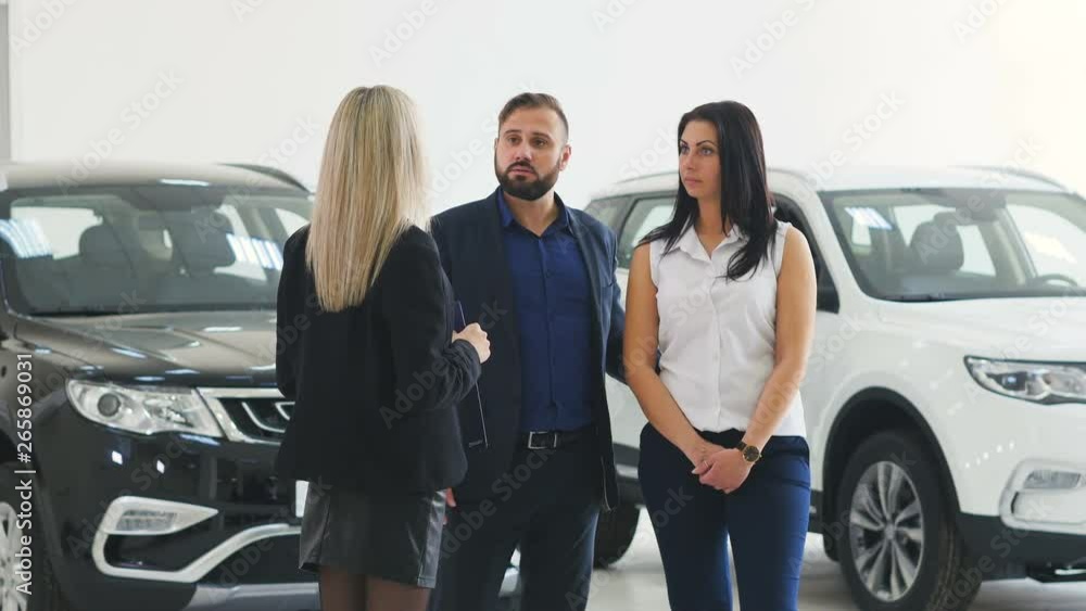 Cavcasian saleswoman with clipboard talking with couple choosing car at dealership Cavcasian saleswoman with clipboard talking with couple choosing car at dealership