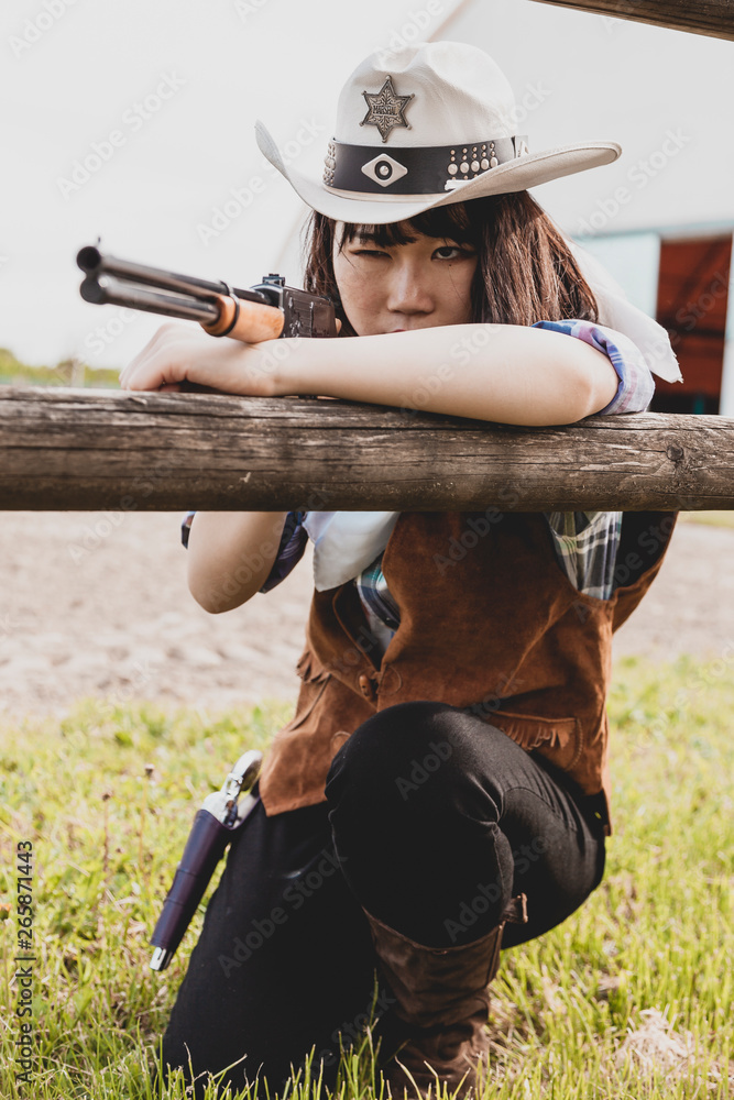 Fototapeta premium Portrait of a beautiful Chinese female cowgirl shooting with a weapon