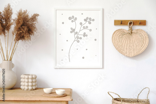 Stylish korean interior of living room with brown mock up poster frame, elegant accessories, flowers in vase, wooden shelf and hanging rattan leaf. Minimalistic concept of home decor. Template. 