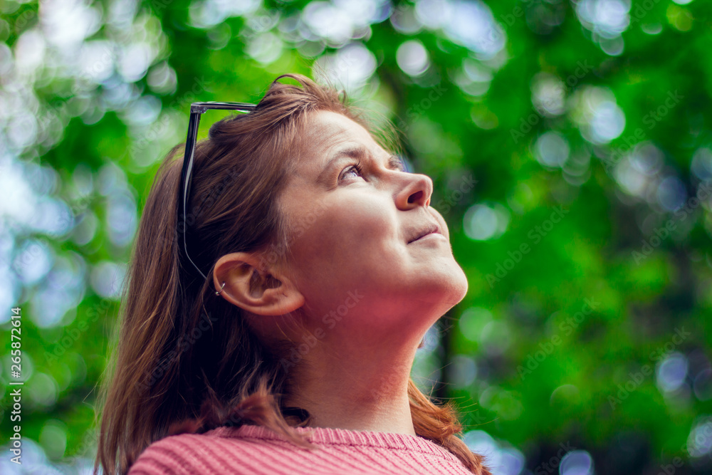 Happy looking young woman wearing a pink blouse with sunglasses on her head daydreaming in the park – Portrait of a smiling girl thinking and contemplating in nature Happy looking young woman wearing a pink blouse with sunglasses on her head daydreaming in the park – Portrait of a smiling girl thinking and contemplating in nature