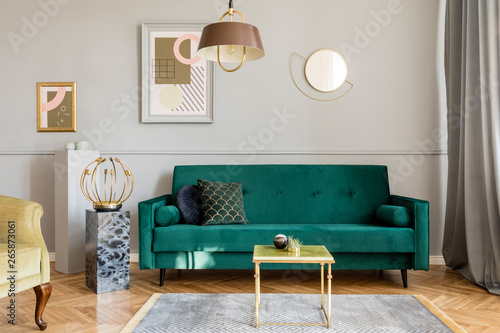 Stylish and luxury living room of apartment interior with elegant green velvet armchair and sofa, coffee table, marble stands, design lamps and chic accessories. Abstract paintings on the gray wall.  © FollowTheFlow