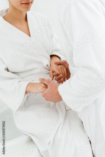 cropped view of man holding hands with young woman in bathrobe