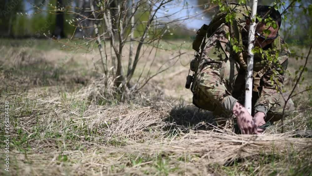 A warrior or military soldier dressed in camouflage tie a mine trap or land mine to a tree trunk