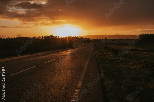 Misterious road during sunrise with a car going in the background.