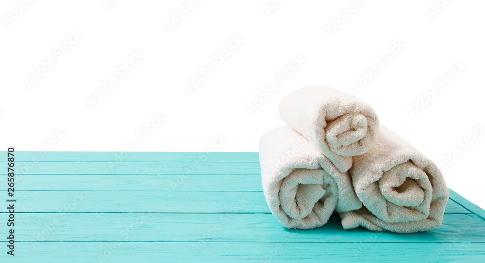Fototapeta premium Rolled white towels on blue wooden table isolated on white background. Copy space and top view. Bathroom objects for shower body treatment. Selective focus. Banner