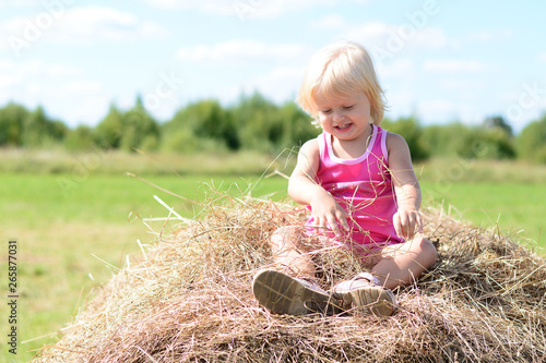 Happy baby girl laughing on summer haystack