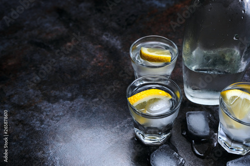 Vodka. Shots, glasses with vodka and lemon with ice .Dark stone background.