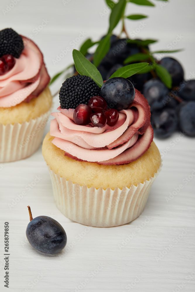 selective focus of cupcakes with cream and grapes on white surface