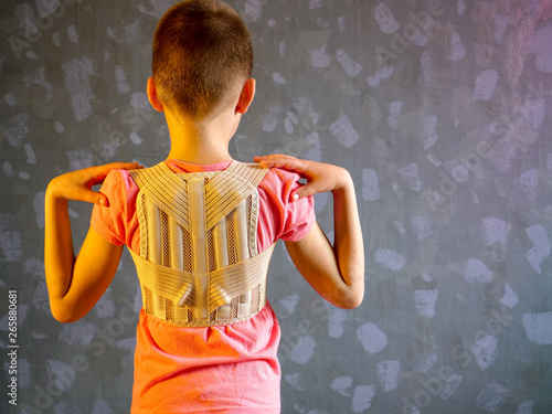 Kid in corrector for spine in pink t-shirt on a gray background .Child wearing back support belt for support and improve back posture photo