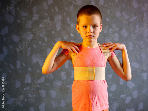 Kid in corrector for spine in pink t-shirt on a gray background .Child wearing back support belt for support and improve back posture photo