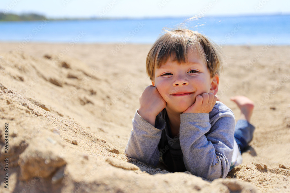 Ein dreijähriger Junge liegt im Sand Ein dreijähriger Junge liegt im Sand
