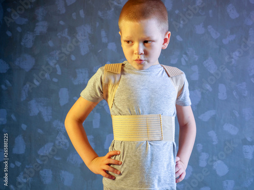 Kid in corrector for spine in gray t-shirt on a gray background .Child wearing back support belt for support and improve back posture photo