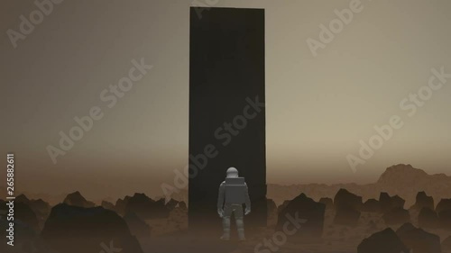 Astronaut walking on the surface of a Mars like planet stops and a Monolith constructs itself in front of him. This version does not have the light emanating from it. photo