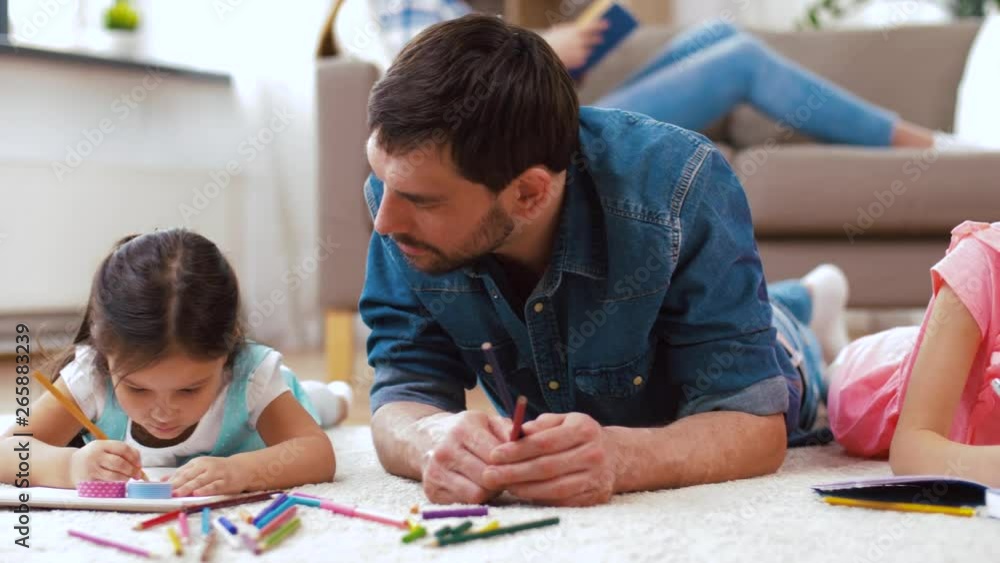 family, fatherhood and leisure concept - father spending time with his little daughters drawing in sketchbooks by crayons and lying on floor at home family, fatherhood and leisure concept - father spending time with his little daughters drawing in sketchbooks by crayons and lying on floor at home