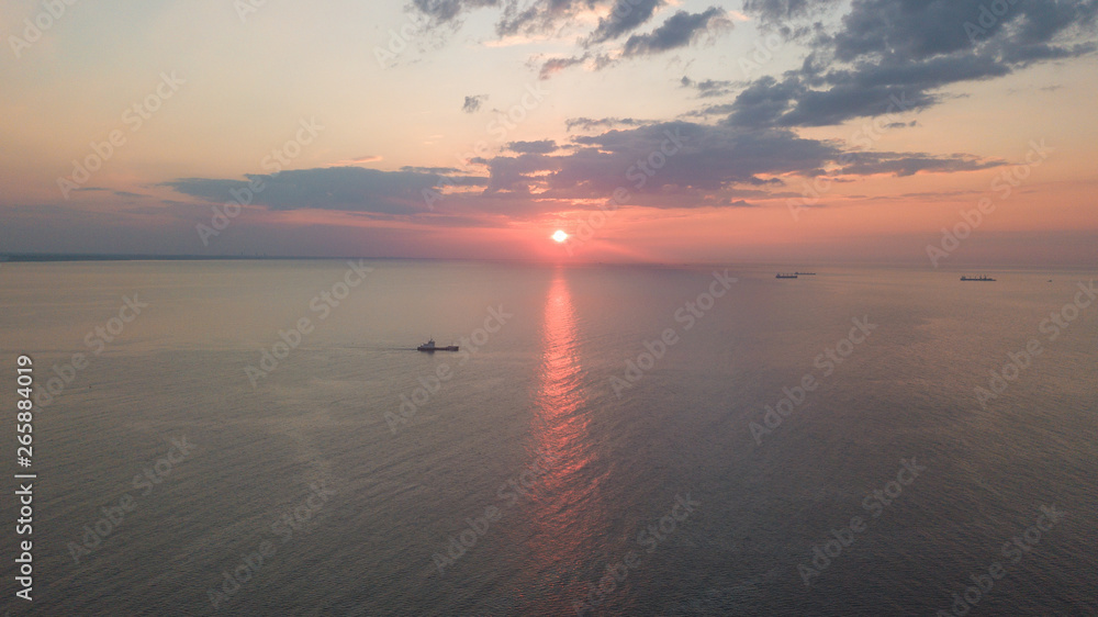 Naklejka premium Dawn on the sea. The warm sun rises above the water. Photographed from the drone. Aerial photo shooting