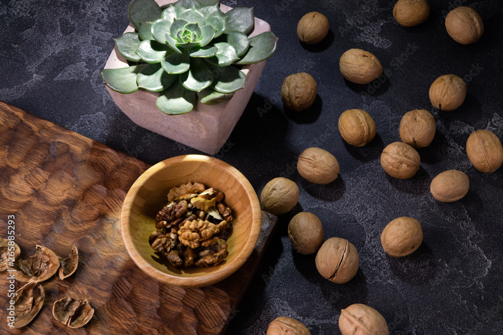 Walnut kernels in wooden bowl, whole walnuts and Echeveria plant on blue slate table. Healthy nuts and seeds composition.