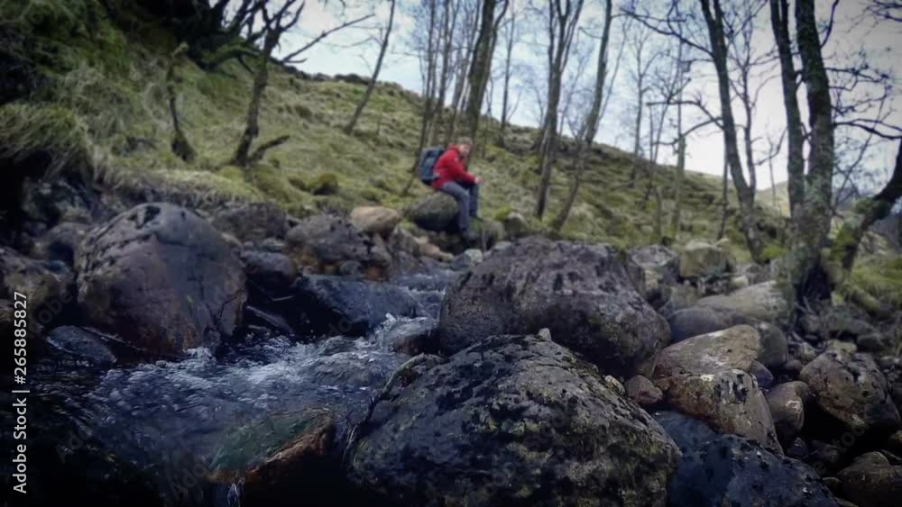 Trekker sitting on wet stones near brook in spring while on hike Trekker sitting on wet stones near brook in spring while on hike