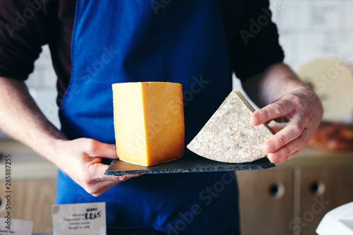 Midsection of cheesemonger holding slate of two different cheeses photo