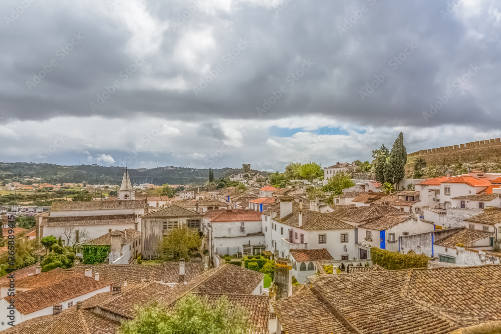 View of the fortress and Luso Roman castle of Óbidos, with buildings of Portuguese vernacular architecture and sky with clouds, in Portugal