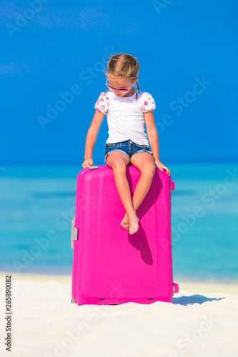 Little adorable girl with big luggage near water villa