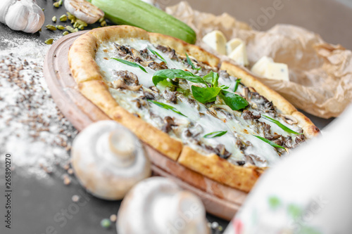Pizza with zucchini, meat, cream cheese on the table in the restaurant. Onion, zucchini, champignons next to the table. Horizontal image. Natural light. Black background. Shallow focus.