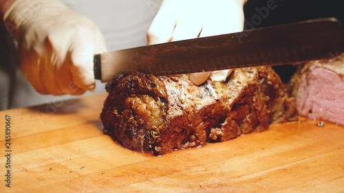 man slices prime rib in slow motion as camera circles. Close up slow motion shot as a chef uses big knife to cut prime rib in the restaurant