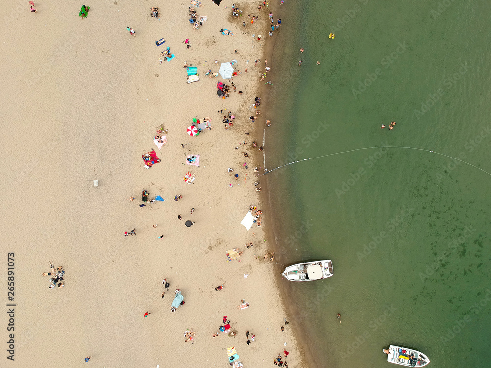 View from above, aerial view of an Mediterranean sea with a white beach and umbrellas with plenty of tourists who relax and swim. Busy seasonal coast with crowd.