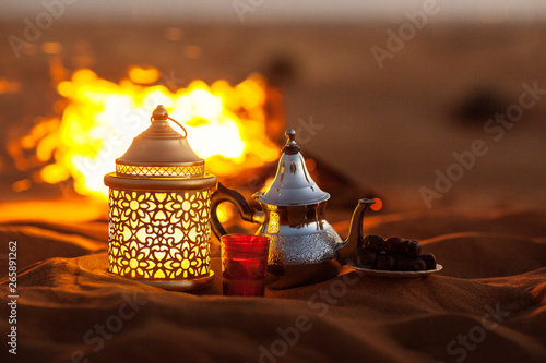 Dates, teapot, cup with tea near the fire in the desert with a beautiful background. Ramadan Kareem photo