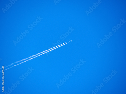 Traces of exhaust gases from the aircraft engine. White stripes and a plane on a bright blue sky. Modern jet plane with white condensation track. Travel concept. Beautiful background or wallpaper.