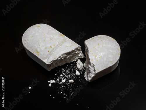 Close-up of white herbal opioid pills. Macro shot of white oval broken tablet on black mirror surface. Smallest structure elements particles visible. Medicine concept theme background with copy space.