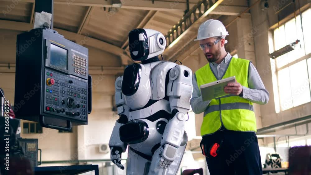 Person checks working robot, standing in a factory room. Person checks working robot, standing in a factory room.