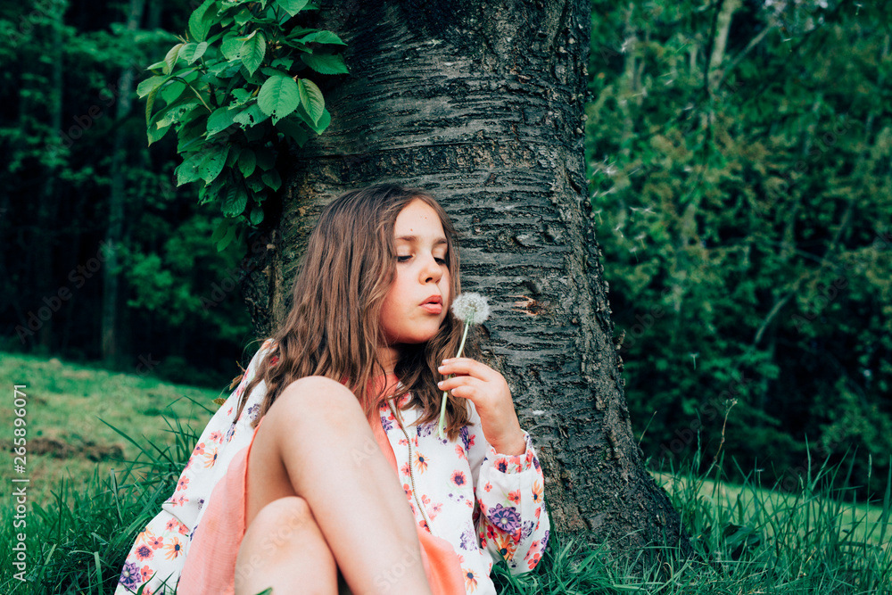 Portrait of girl sitting on a meadow blowing dandelion