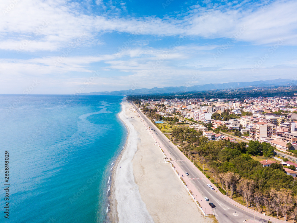 Panoramica aerea del lungomare di Locri, in Calabria. La spiaggia bianca, il mare Mediterraneo blu e le case della città.